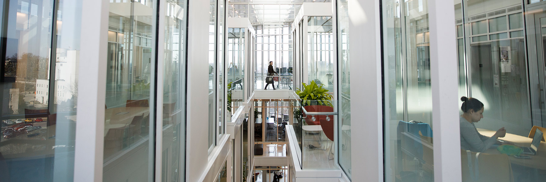 A photo that looks past the glass conference rooms in Luddy Hall to show a woman passing through a hallway.